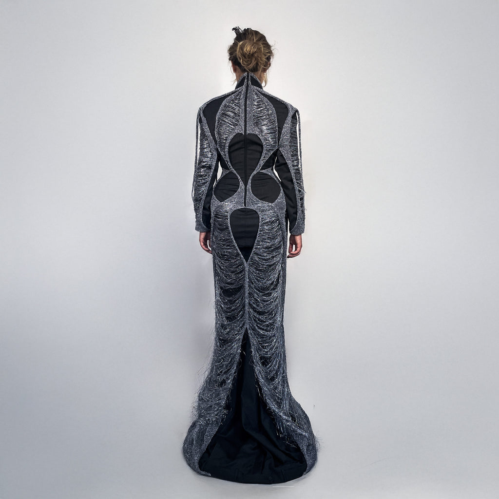 Woman wearing a long, dark gray dress layered with metallic knit on a light gray background 