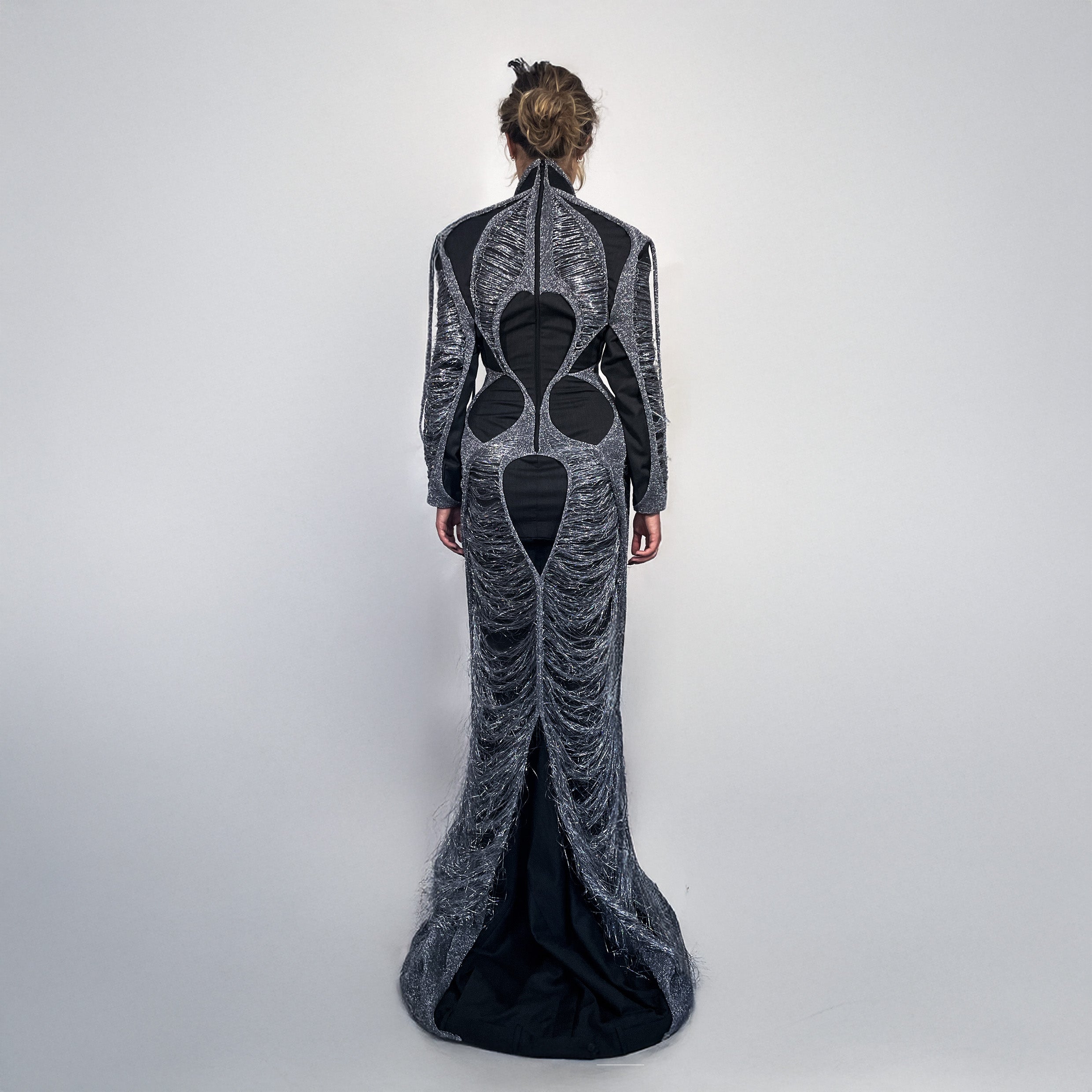 Woman wearing a long, dark gray dress layered with metallic knit on a light gray background 