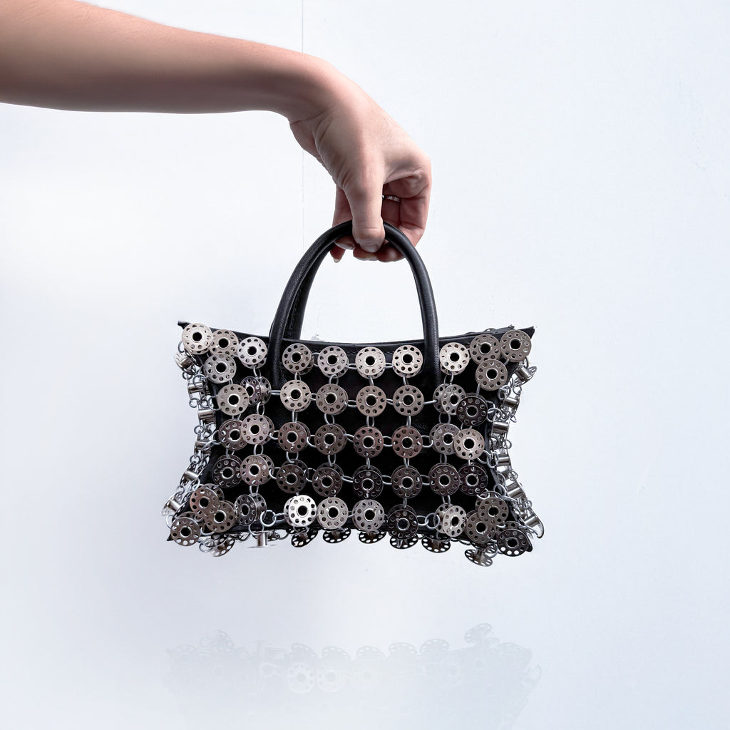 small black leather star shaped handbag layered with metal bobbins on light gray background 