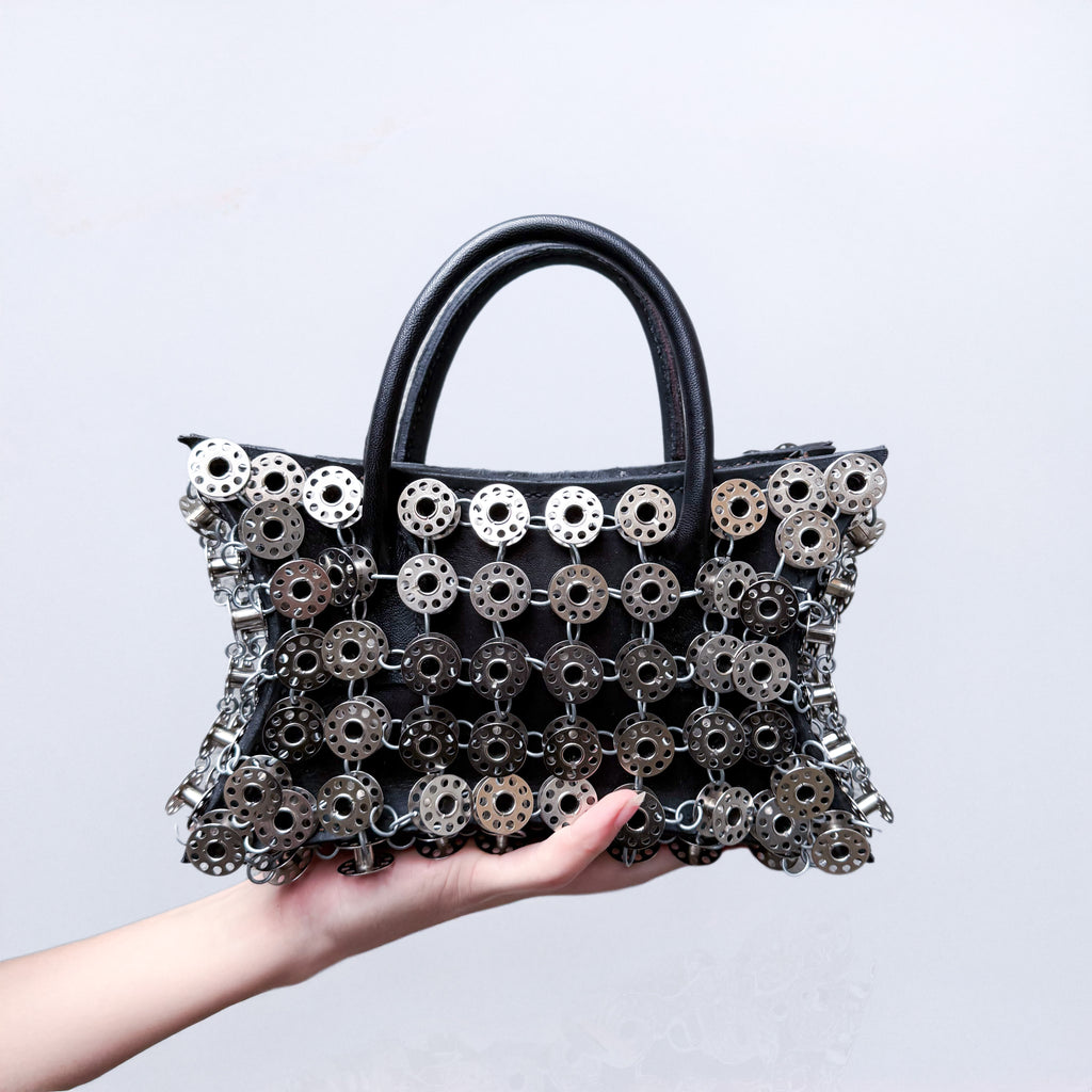 small black leather star shaped handbag layered with metal bobbins on light gray background 