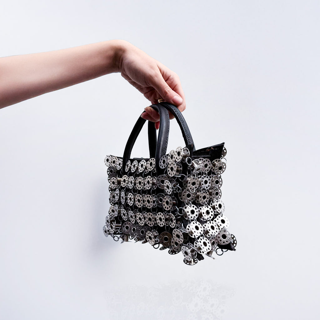 small black leather star shaped handbag layered with metal bobbins on light gray background 
