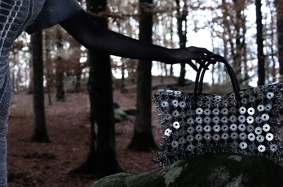 Person in a sequined outfit standing in a forest with a sequined bag.