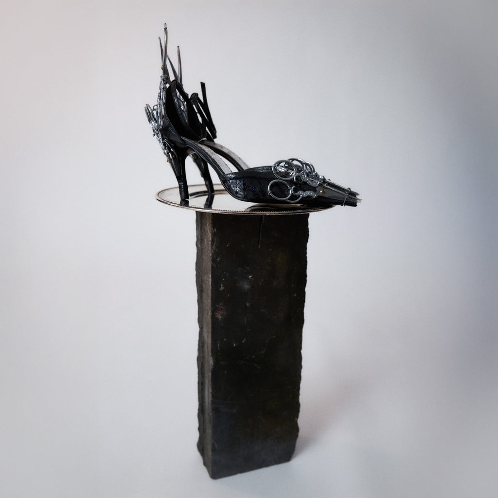 upcycled leather black heels adorned with metal scissors set on a light gray background. 
